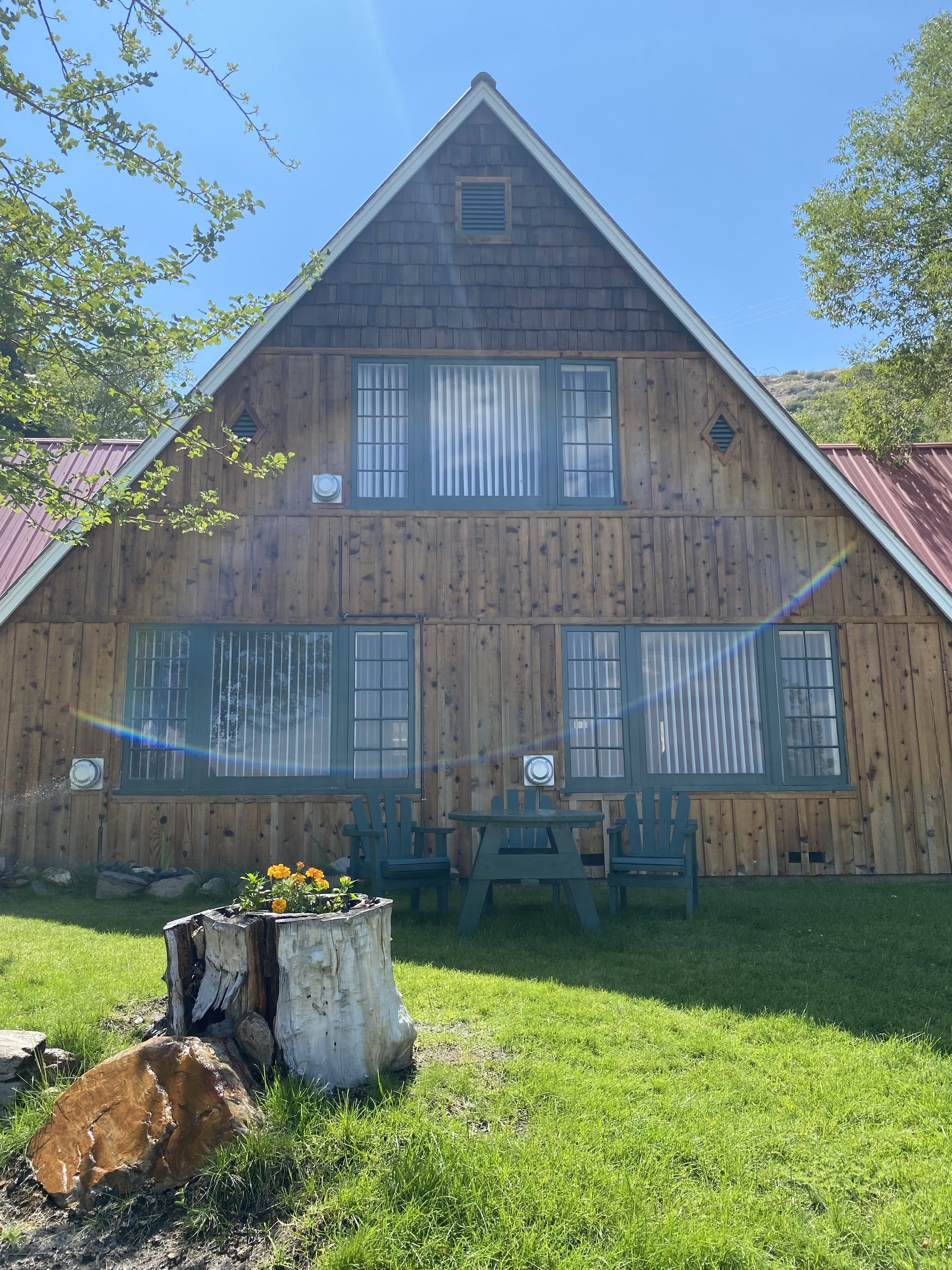 Une grange en bois avec un toit en pente, de grandes fenêtres et une table de pique-nique avec des chaises.