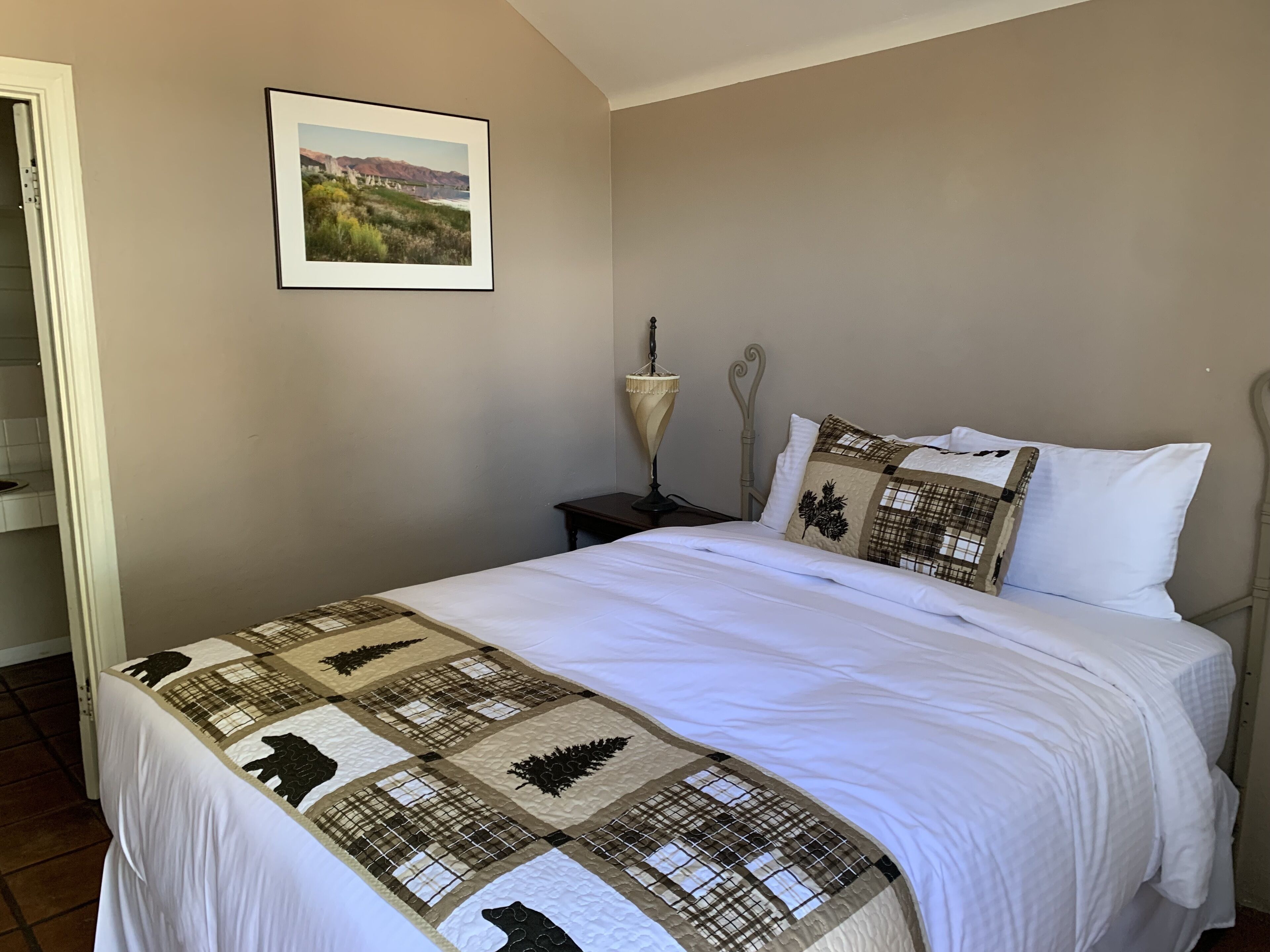 A bedroom with a bed, a nightstand, a lamp, and a framed picture on the wall.