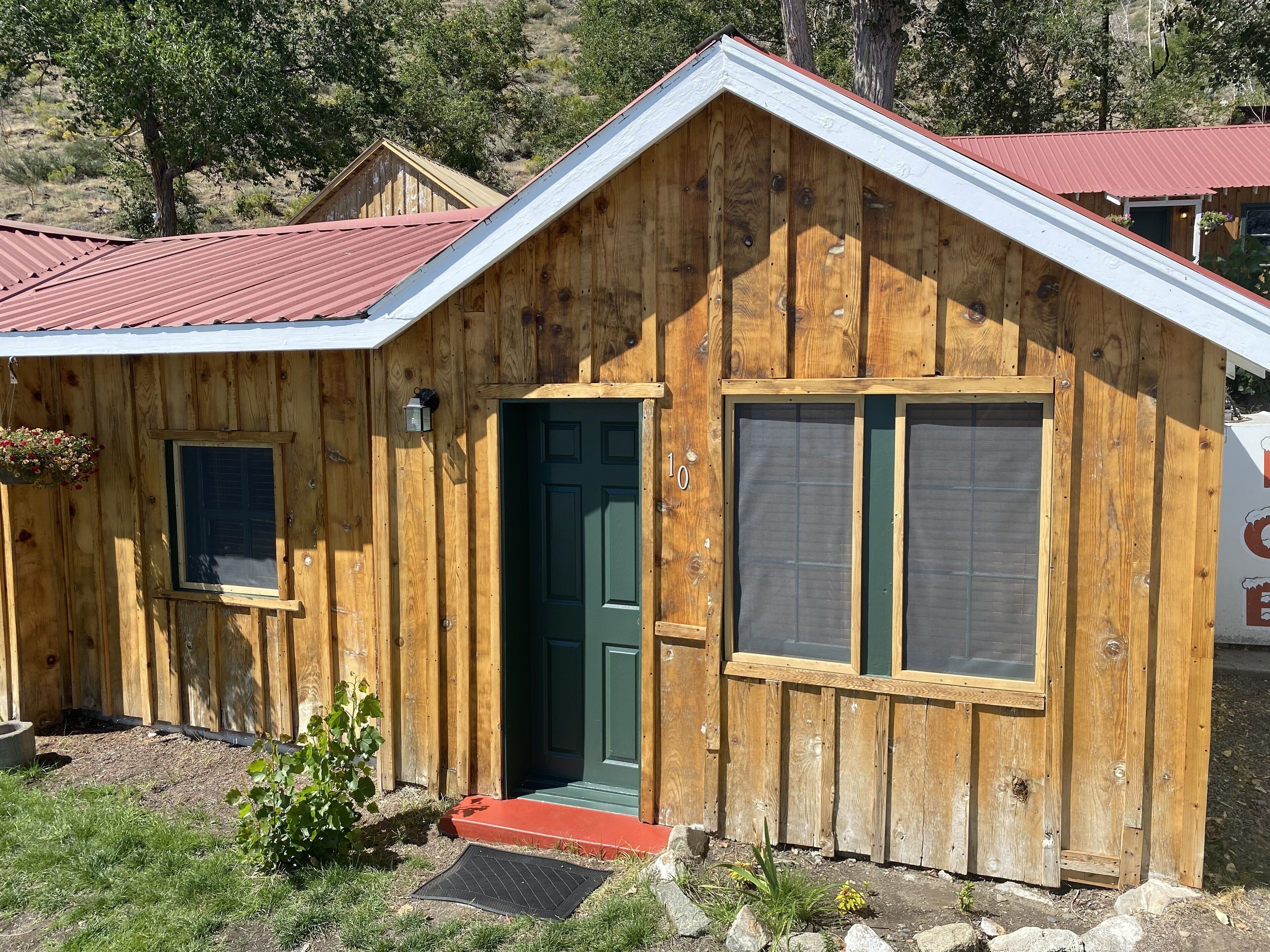 A wooden cabin with a green door, a small window, and a red roof.