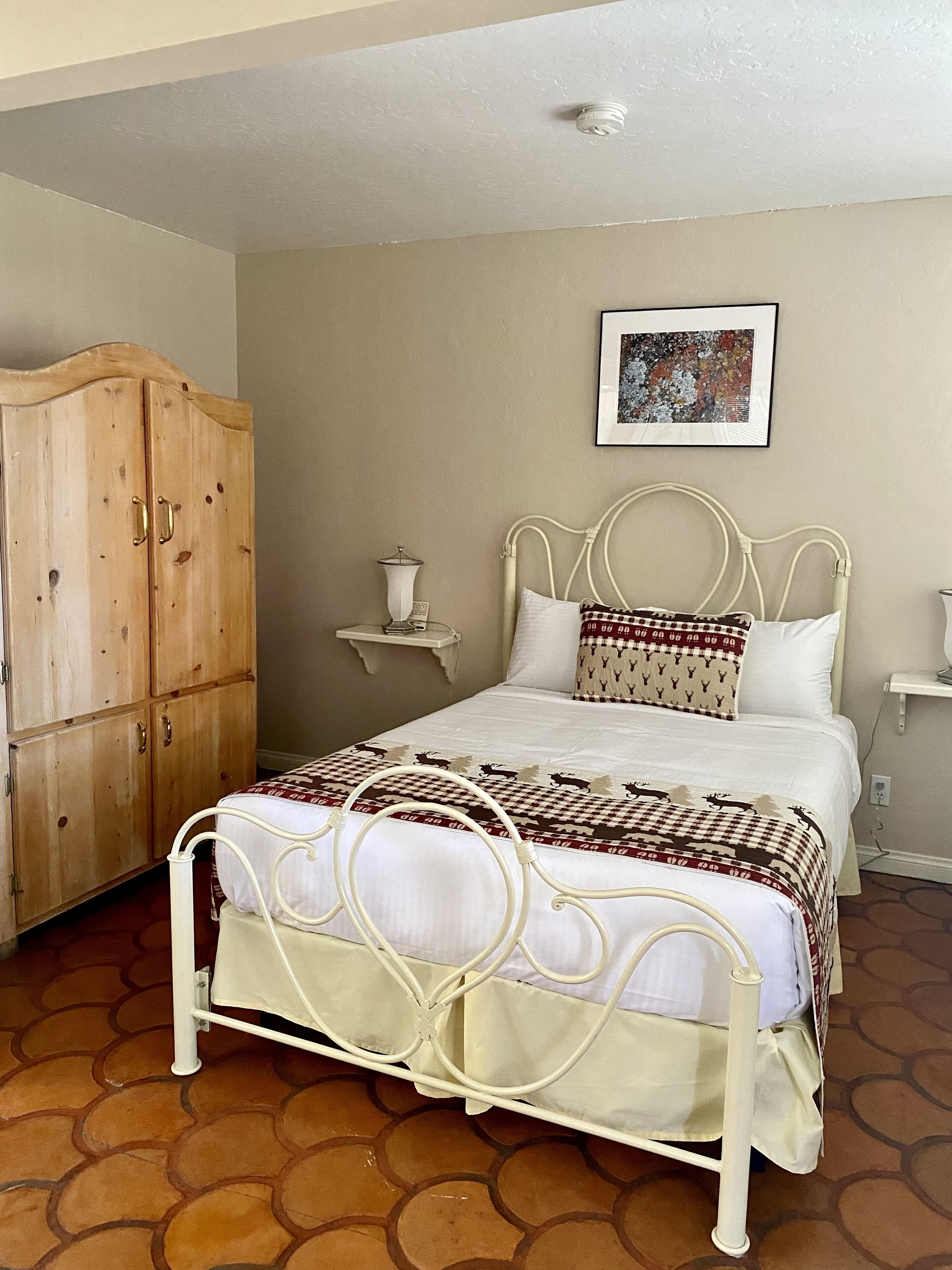 A bedroom with a bed, a wooden wardrobe, a bedside table, and a wall-mounted picture.