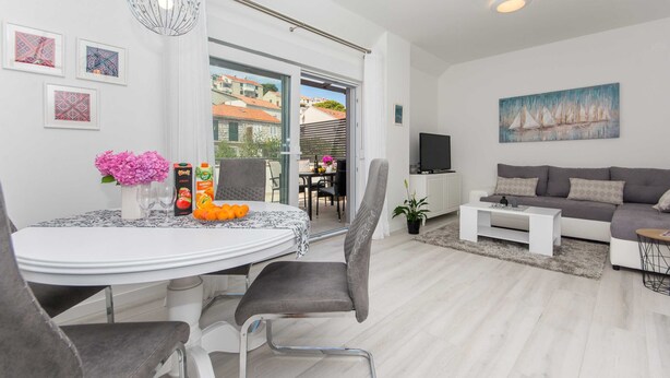 A modern living room with a sofa, a coffee table, and a dining area with a table and chairs. - Apartment Gloria (Dubrovnik)