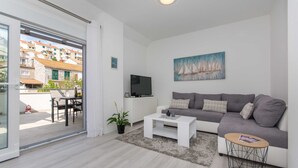 A modern living room with a grey sofa, a white coffee table, and a painting of sailboats. - Apartment Gloria (Dubrovnik)