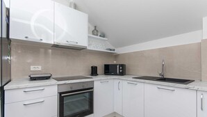 A modern kitchen with white cabinets, a built-in oven, a microwave, and a double sink. - Apartment Gloria (Dubrovnik)