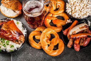 Diversos alimentos como pretzels, salchichas y una pierna de cerdo asada, sugiriendo una comida temática alemana.