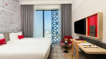 A hotel room with a large bed, a desk with a chair, a TV, and a view of the cityscape.