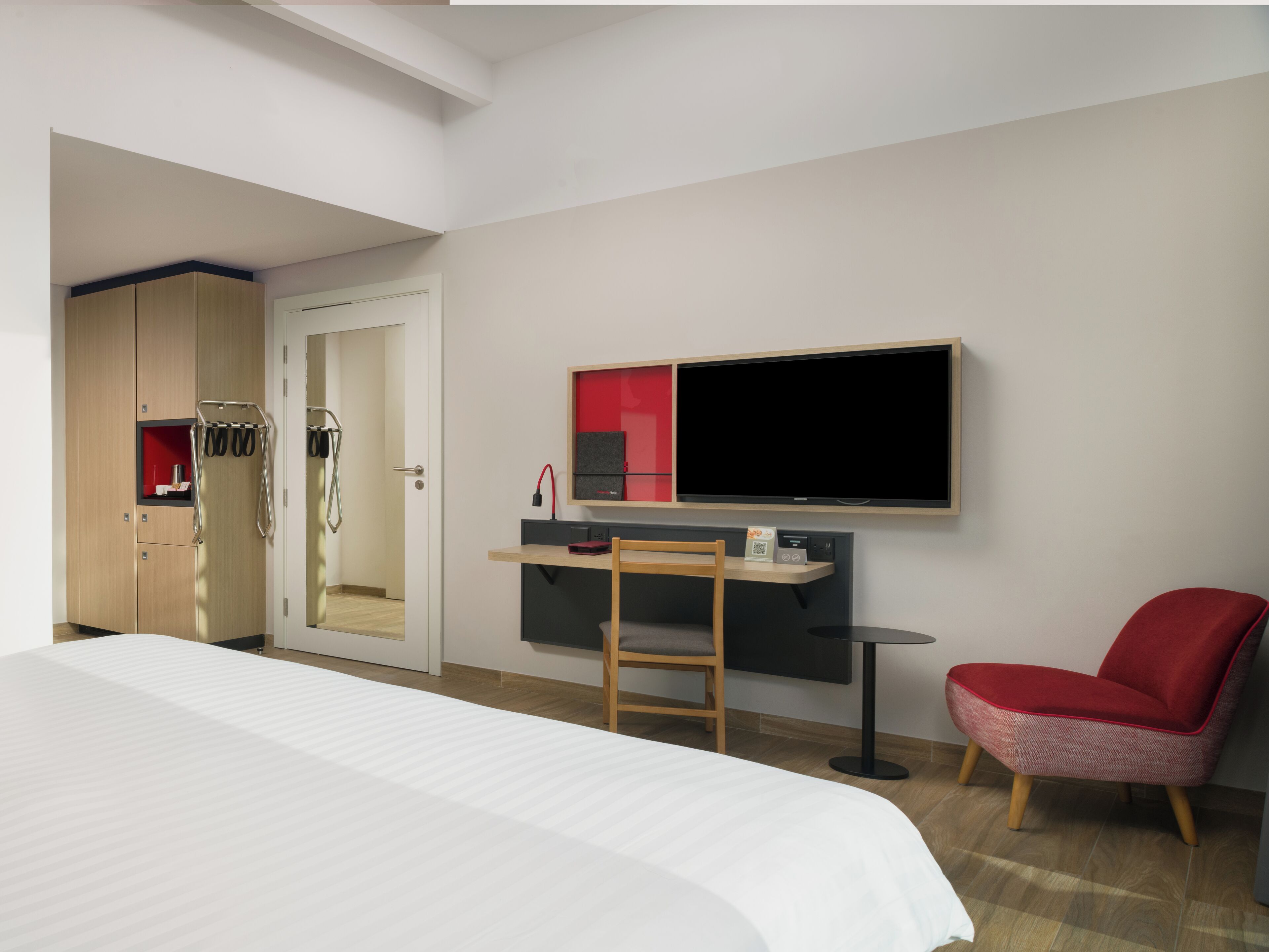A hotel room with a bed, a desk, a chair, a TV, and a wardrobe.
