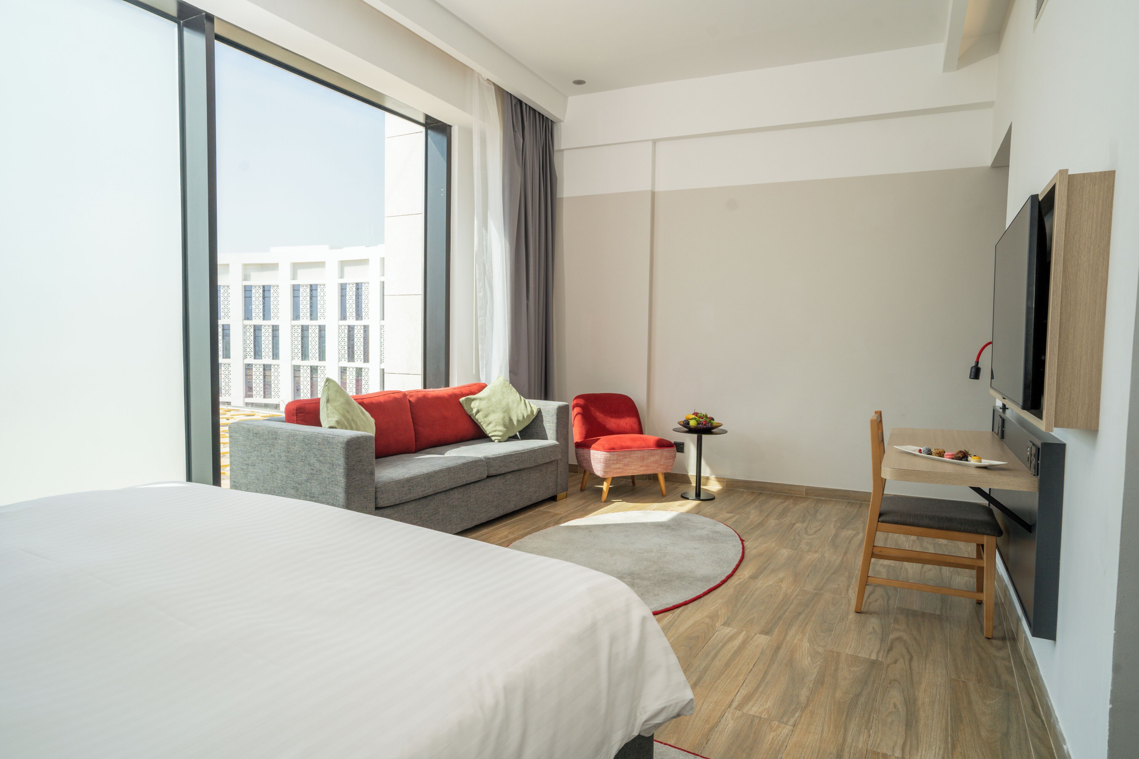 Una habitación de hotel con cama, sofá, sillón, una mesita con fruta y televisor.