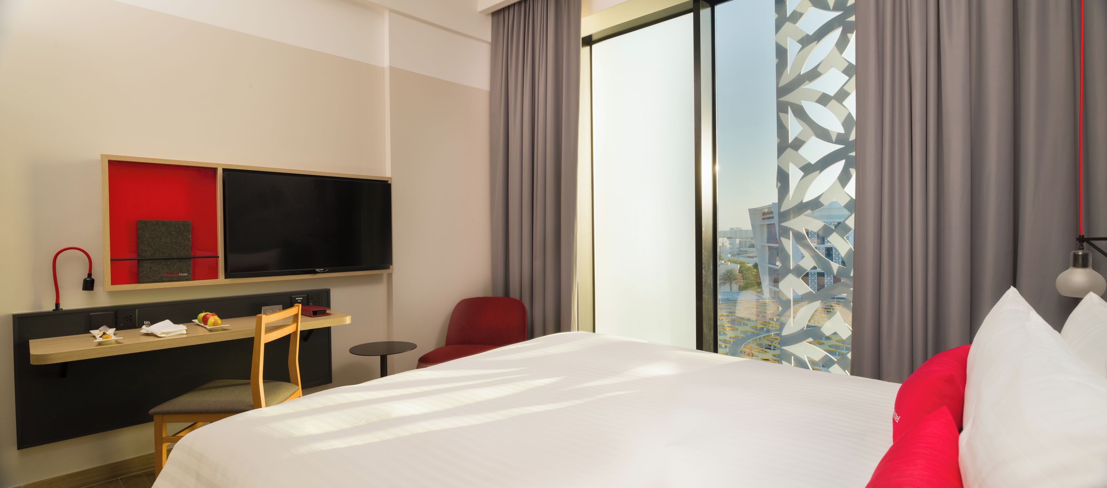 Una habitación de hotel con cama, escritorio con silla, televisor y ventana con cortinas.