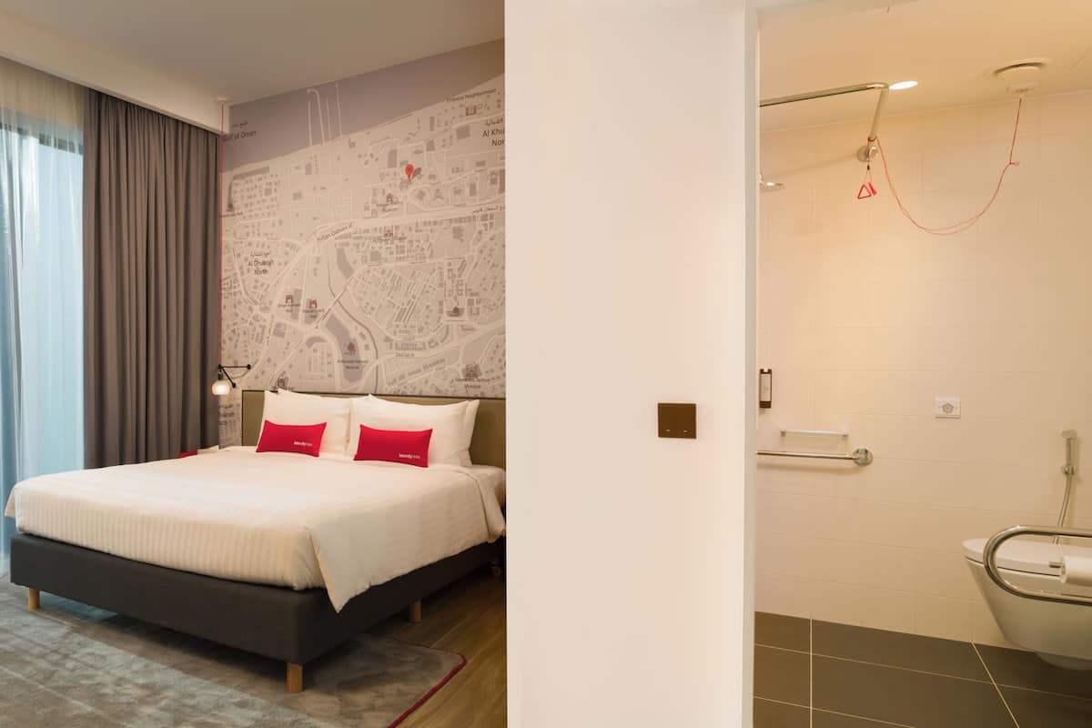 Ein modernes Hotelzimmer mit einem großen Bett, einer Karte an der Wand und einem Badezimmer mit Dusche und Toilette.