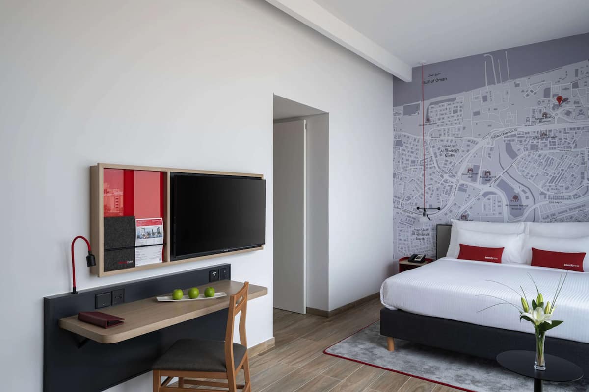 Ein Hotelzimmer mit einem Bett, einem Schreibtisch mit Flachbildfernseher, einer Karte an der Wand und einem kleinen Tisch mit Äpfeln.