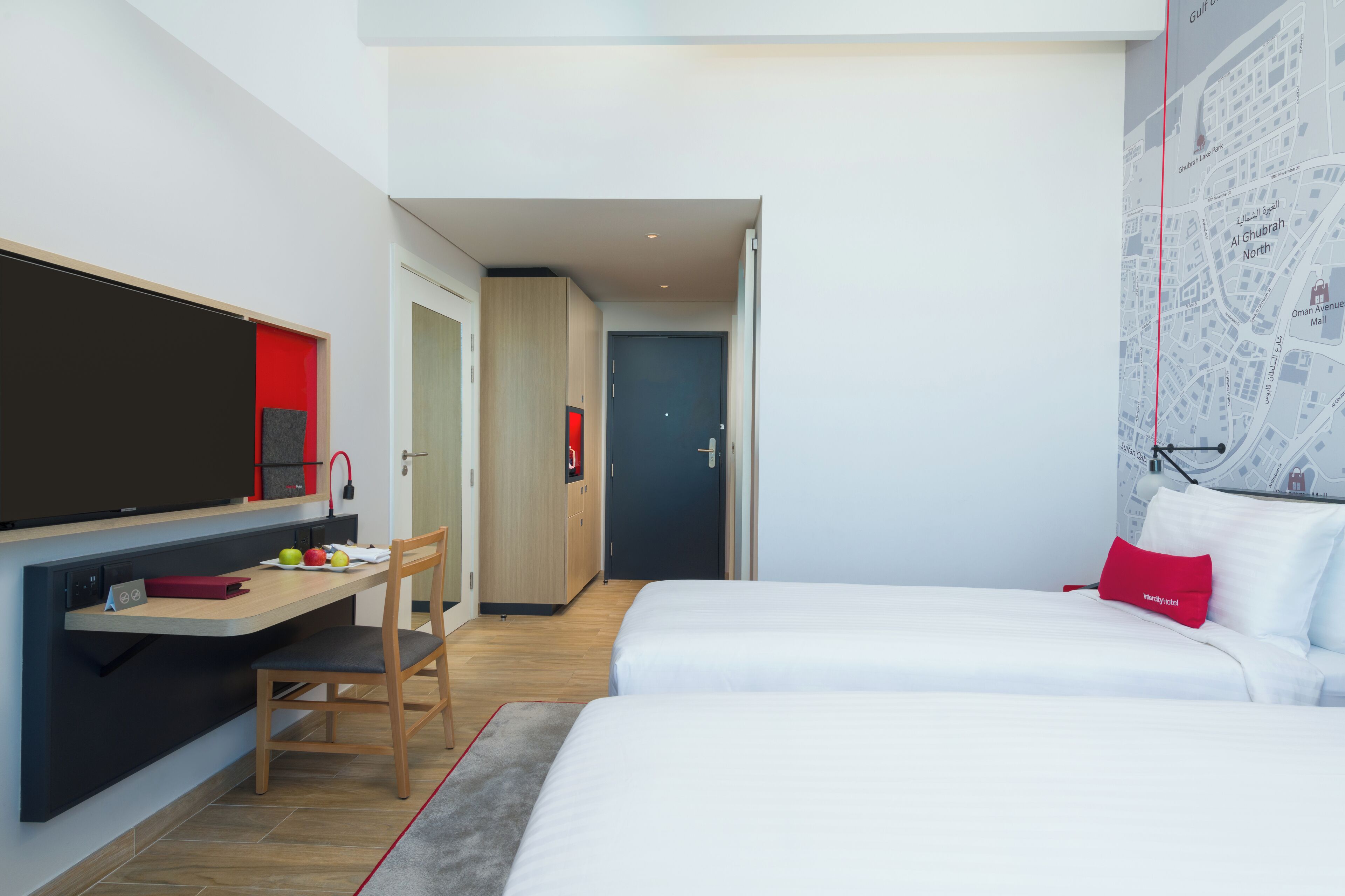 Een moderne hotelkamer met een bureau, twee bedden, een televisie en een kaart aan de muur.