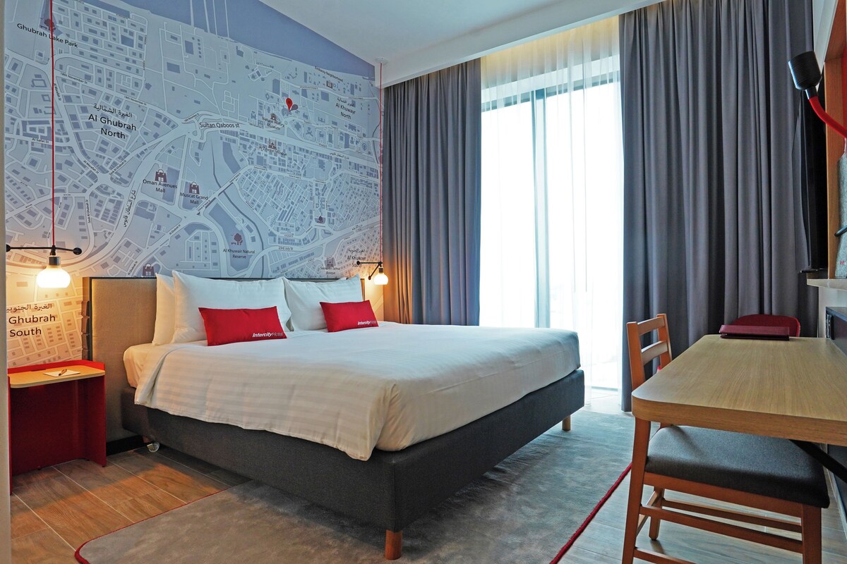 A hotel room with a large bed, a desk, and a map on the wall.