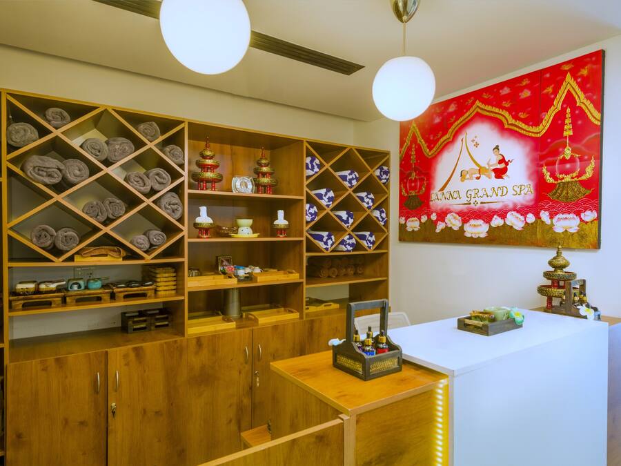 A hotel lobby with wooden shelving displaying towels and decorative items, a reception desk with a small shrine, and a large red wall painting.