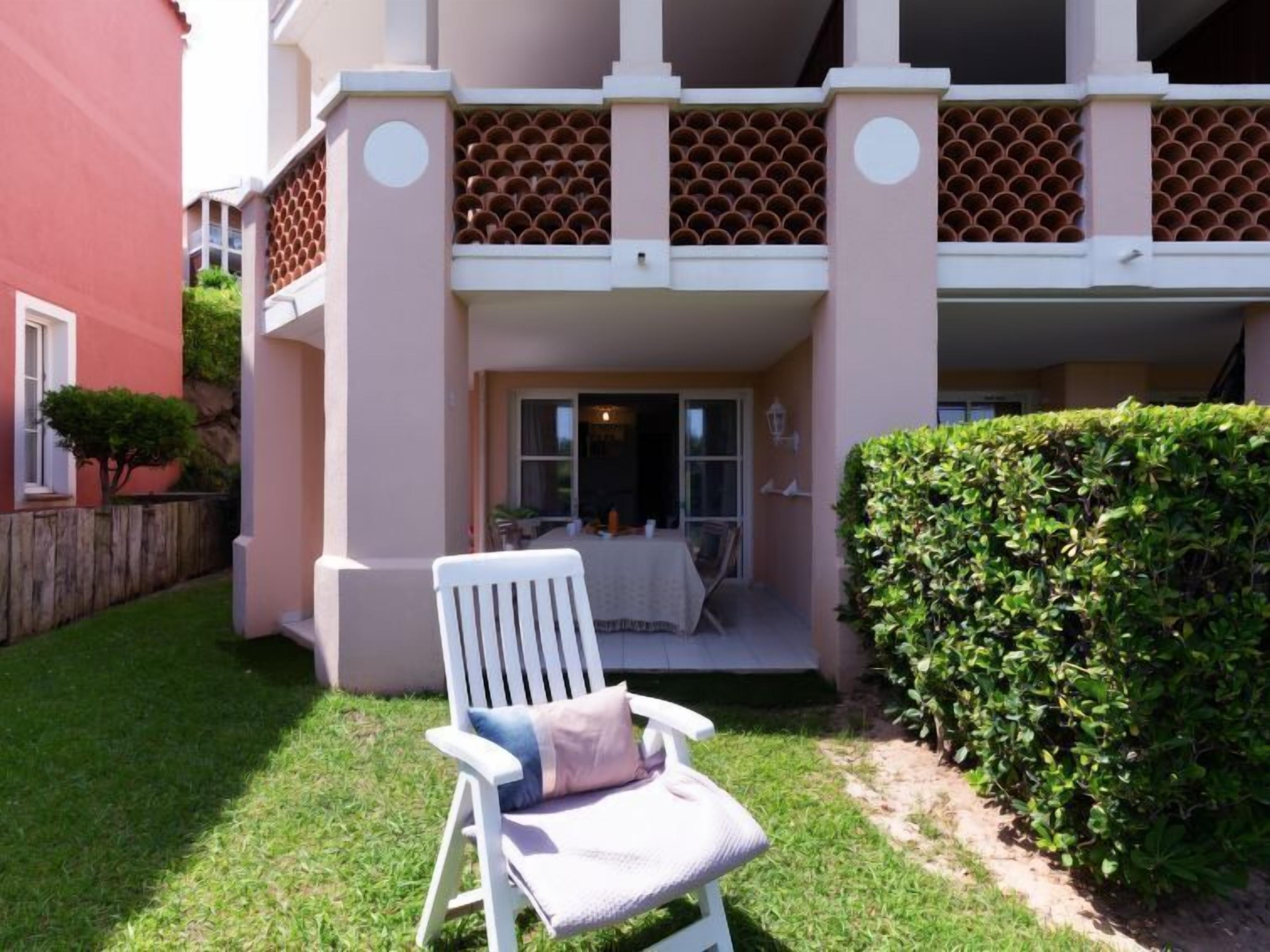 Un bâtiment à deux étages doté d’un patio couvert, d’une chaise blanche et d’une haie bien entretenue.