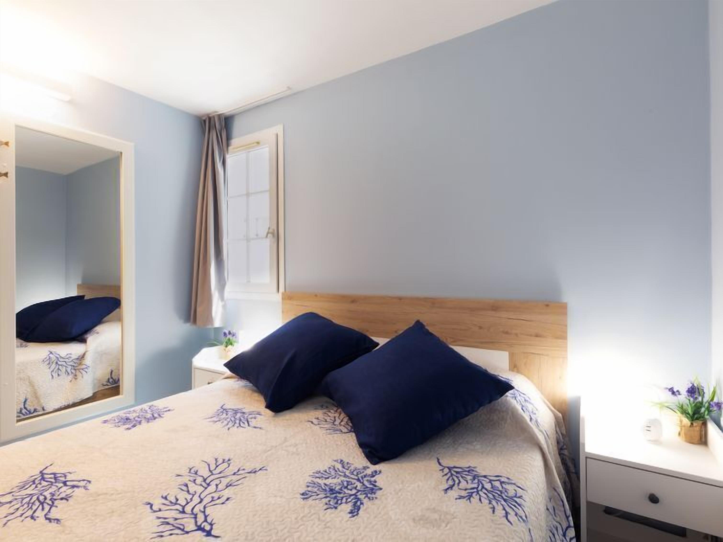 A bedroom with a bed, a nightstand, a mirror, and a window with curtains.