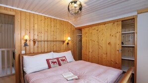 A wooden-paneled bedroom with a bed, two wall-mounted lamps, and a ceiling light fixture. - Cheechako by Interhome (Nendaz)