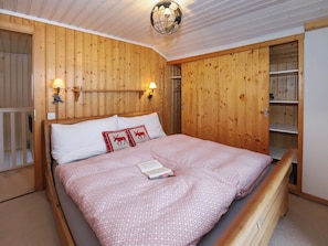 Quarto com painéis de madeira, uma cama, duas luminárias na parede e um lustre.