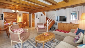 A cozy living room with wooden beams, a dining area with striped chairs, a staircase, and a TV in the living room. - Cheechako by Interhome (Nendaz)
