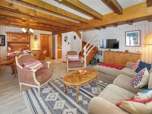Uma sala de estar acolhedora com vigas de madeira, um espaço de refeições com cadeiras listradas, uma escada e uma TV na sala.