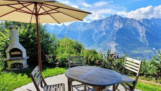 An outdoor patio with a round table and four chairs, a wooden pizza oven, and a large umbrella. - Cheechako by Interhome (Nendaz)