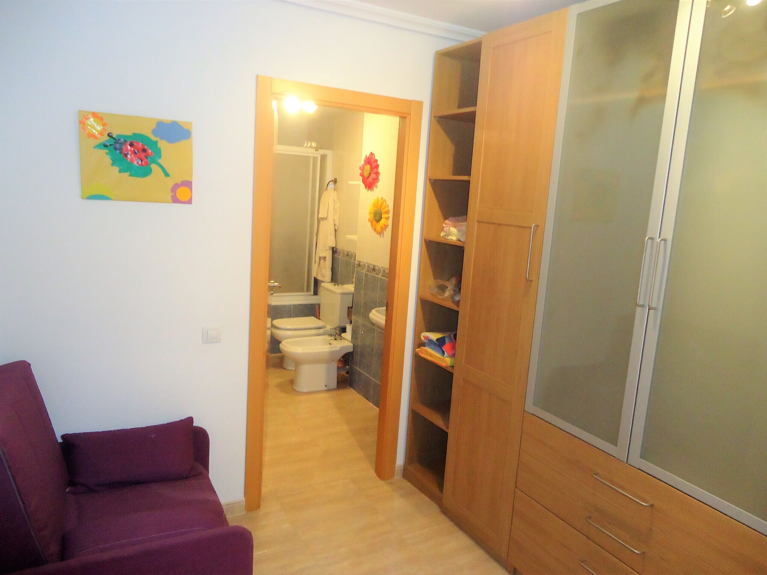 A room with a wooden wardrobe, a purple sofa, and a bathroom visible through an open door.