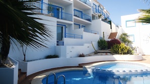 A modern building with balconies, a swimming pool, and surrounding vegetation. - Arabella duplex village (Peñiscola)