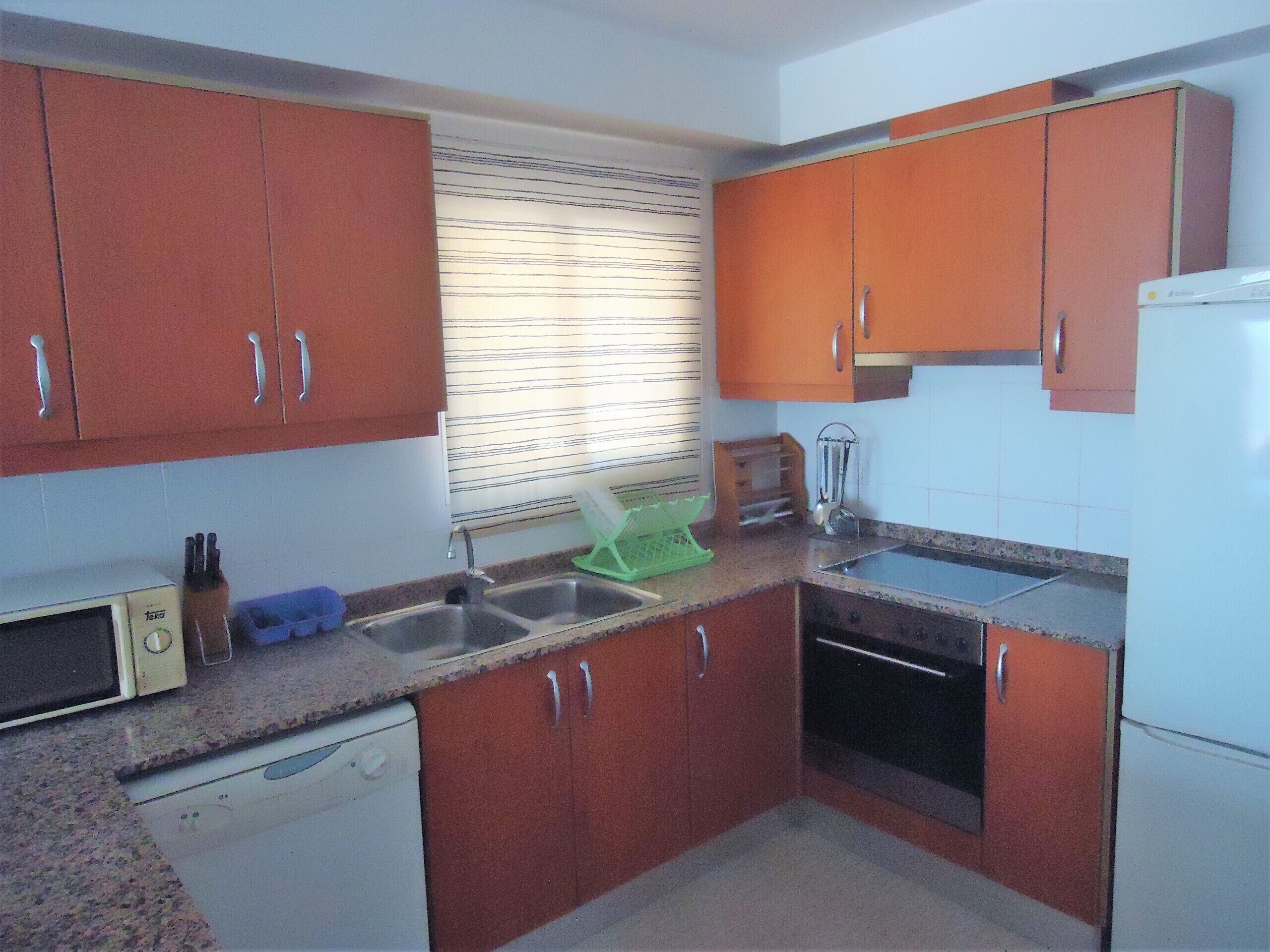 A compact kitchen with brown cabinets, a white dishwasher, a sink, and a stove.
