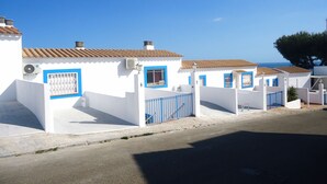 A row of white buildings with blue doors and windows, a clear blue sky, and a tree in the background. - Arabella duplex village (Peñiscola)