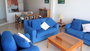 A living room with blue sofas, a wooden coffee table, and a dining area with a table and chairs. - Arabella duplex village (Peñiscola)