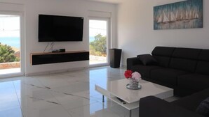 A modern living room with a flat-screen TV, a black sofa, a coffee table with a vase, and a painting on the wall.