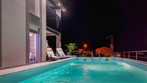A nighttime swimming pool area with lounge chairs and a building with a balcony.