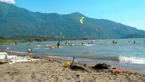 Ein Strand mit Menschen, die sich an Wassersportaktivitäten beteiligen und Drachen steigen lassen, mit Bergen im Hintergrund.
