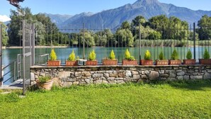 Eine Steinsäule mit Blumentöpfen vor einem See, im Hintergrund Berge.