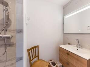 A bathroom with a shower, a wooden chair, and a vanity with a mirror. - Le Rahic by Interhome (Carnac)