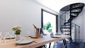 A modern dining area with a wooden table set for two, a metal bucket with a bottle, and a clear chair. - Le Rahic by Interhome (Carnac)