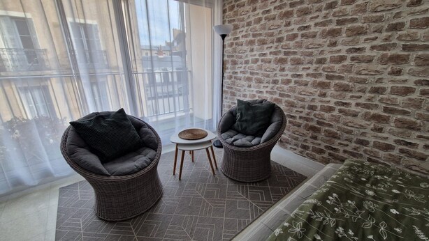 Un balcon avec des fauteuils en osier, une petite table et un mur en briques.