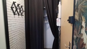 Un couloir étroit avec un rideau noir, un petit tabouret et une porte ornée d’un motif floral.