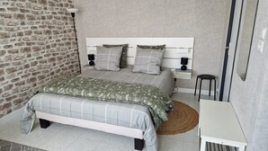 Une chambre avec un mur en briques, un lit avec une tête de lit blanche, deux tables de chevet avec des lampes et une petite table avec une chaise.