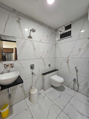 A modern bathroom with a white marble backsplash, a black countertop, a white sink, a toilet, a shower, and a yellow bucket.