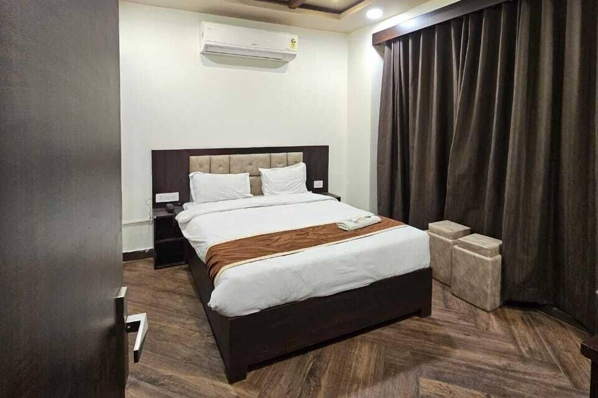 Ein Hotelzimmer mit Holzboden, einem Bett mit weißer Bettwäsche, einem Deckenventilator, einer Klimaanlage und einem dunklen Vorhang.