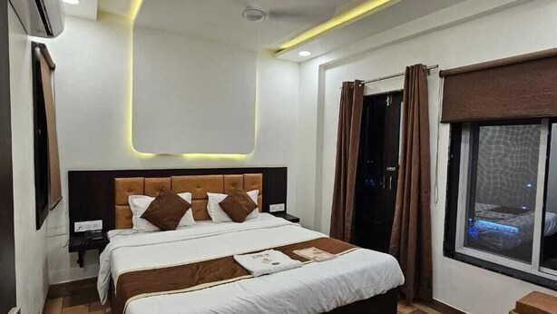Una habitación de hotel moderna con una cama grande, una mesita de noche, un velador, una ventana con cortinas e iluminación empotrada en el techo.