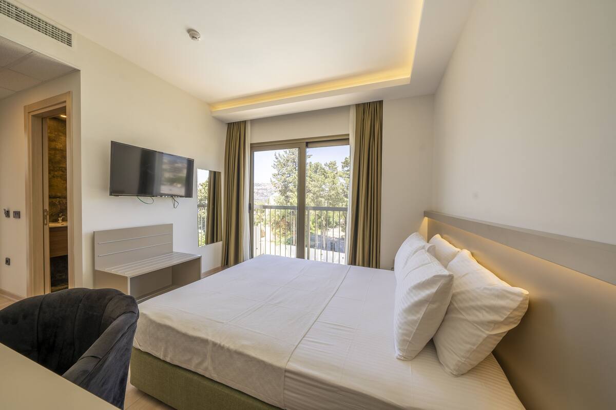 A hotel room with a bed, a TV mounted on the wall, and a window with curtains.
