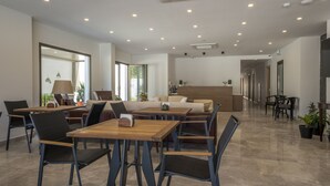 Ein geräumiger, gut beleuchteter Innenbereich mit verschiedenen Sitzgelegenheiten, darunter Tische, Stühle und eine Couch, sowie ein Empfangstresen.