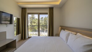 Ein Hotelzimmer mit einem großen Bett, einem an der Wand befestigten Fernseher und einem Balkon mit Vorhängen.