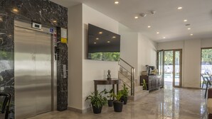 Eine moderne Lobby mit Marmorboden, einer Rezeption, einer Treppe und einem großen Flachbildfernseher an der Wand.