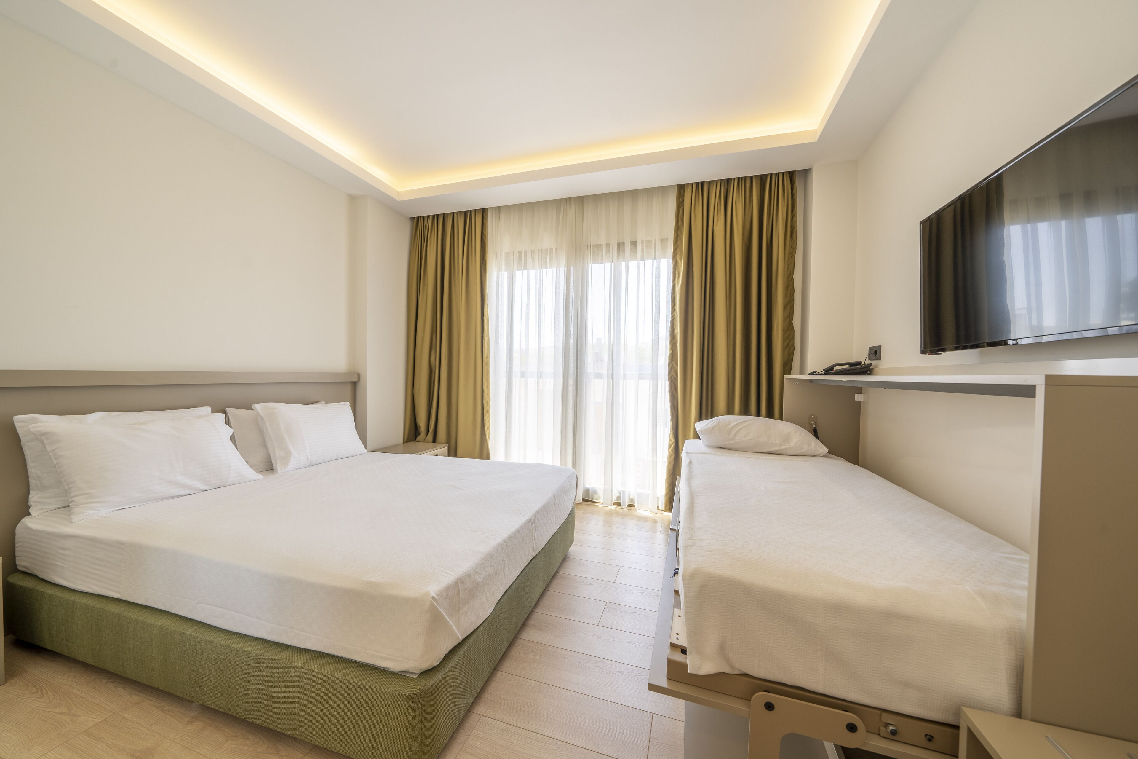 A hotel room with a large bed, a smaller bed, a TV, and a window with curtains.