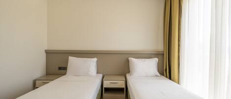A hotel room with two single beds, a nightstand with a clock, and a window with curtains.
