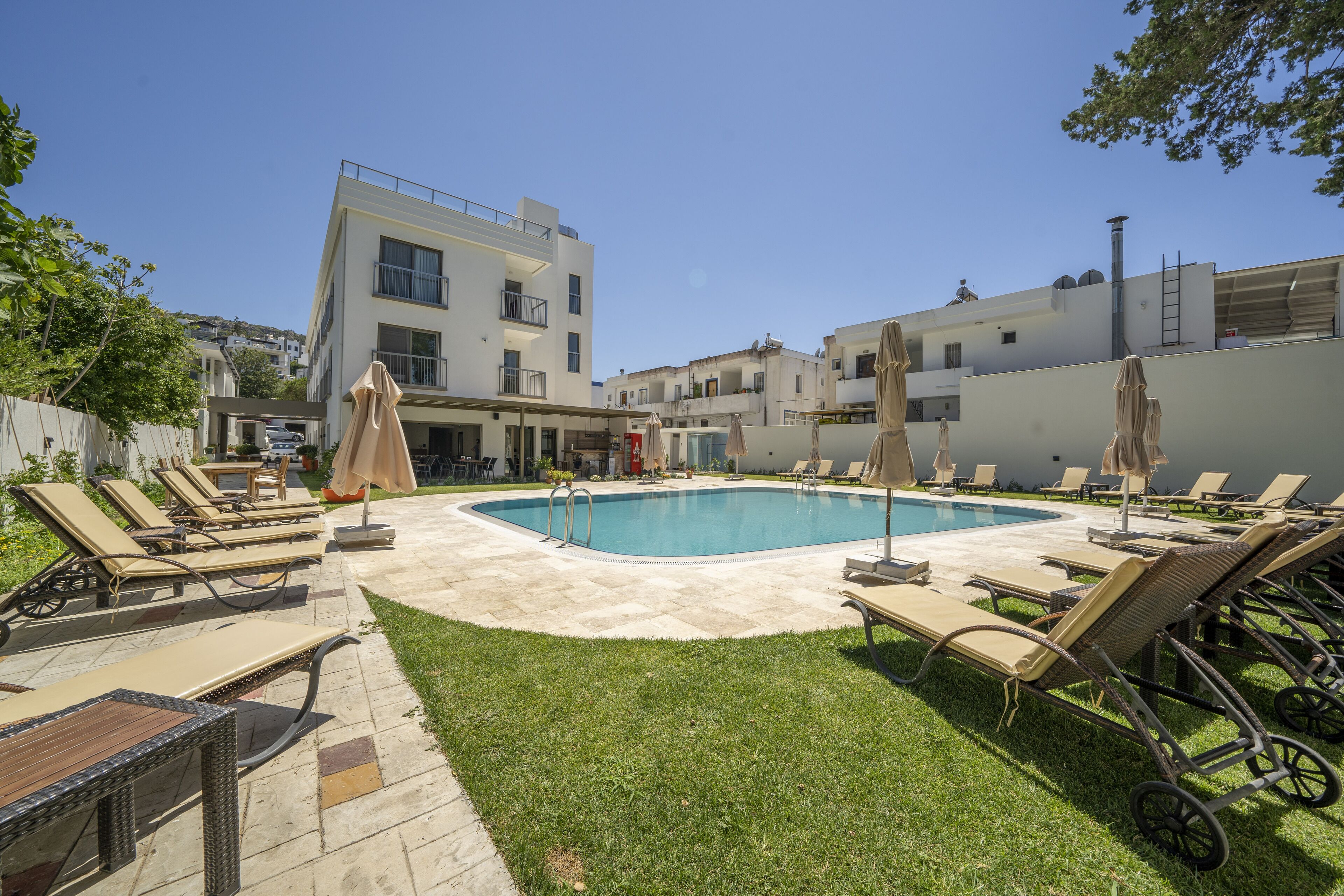 A pool area with lounge chairs and umbrellas, surrounded by a well-maintained lawn and modern buildings.
