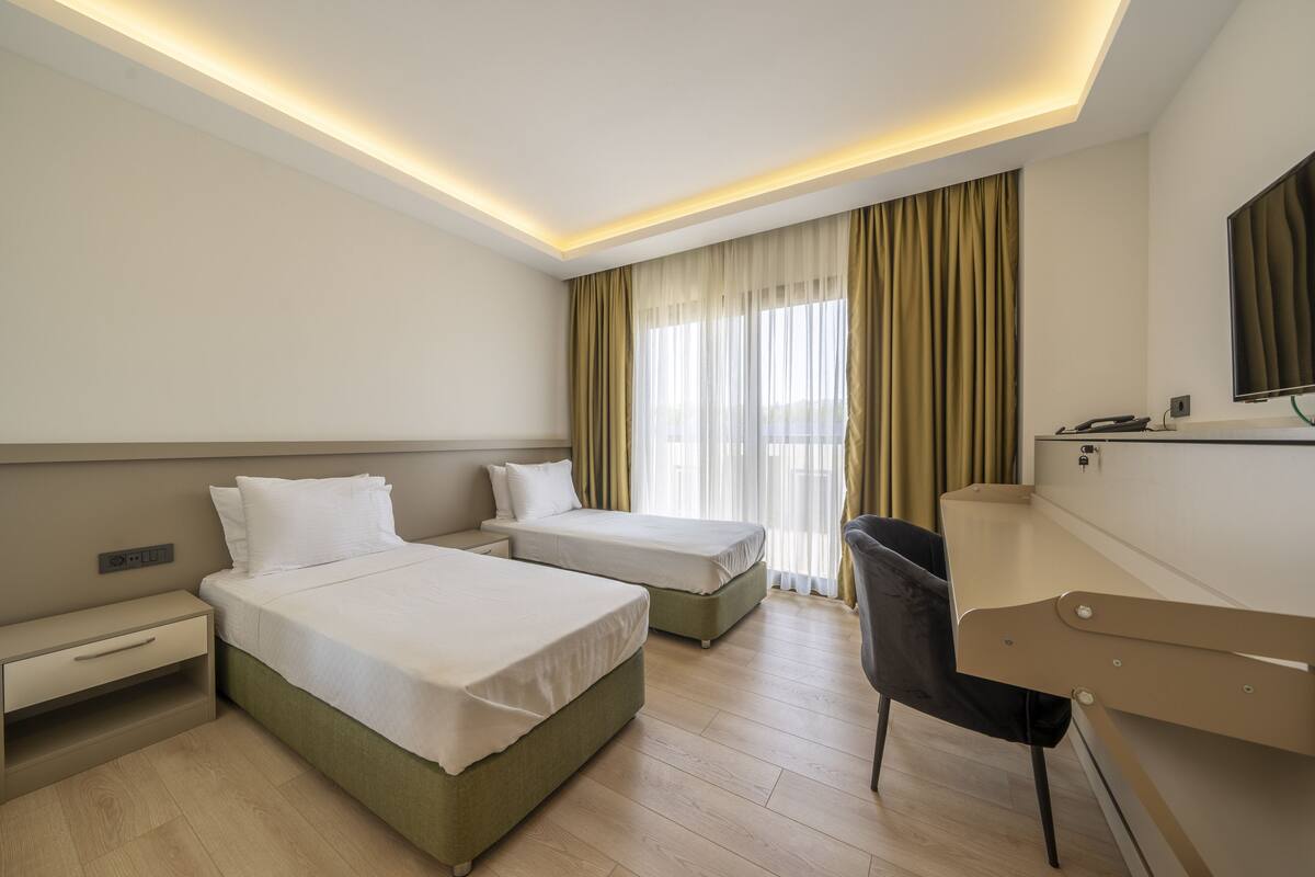 A hotel room with two beds, a desk, a chair, and a TV.