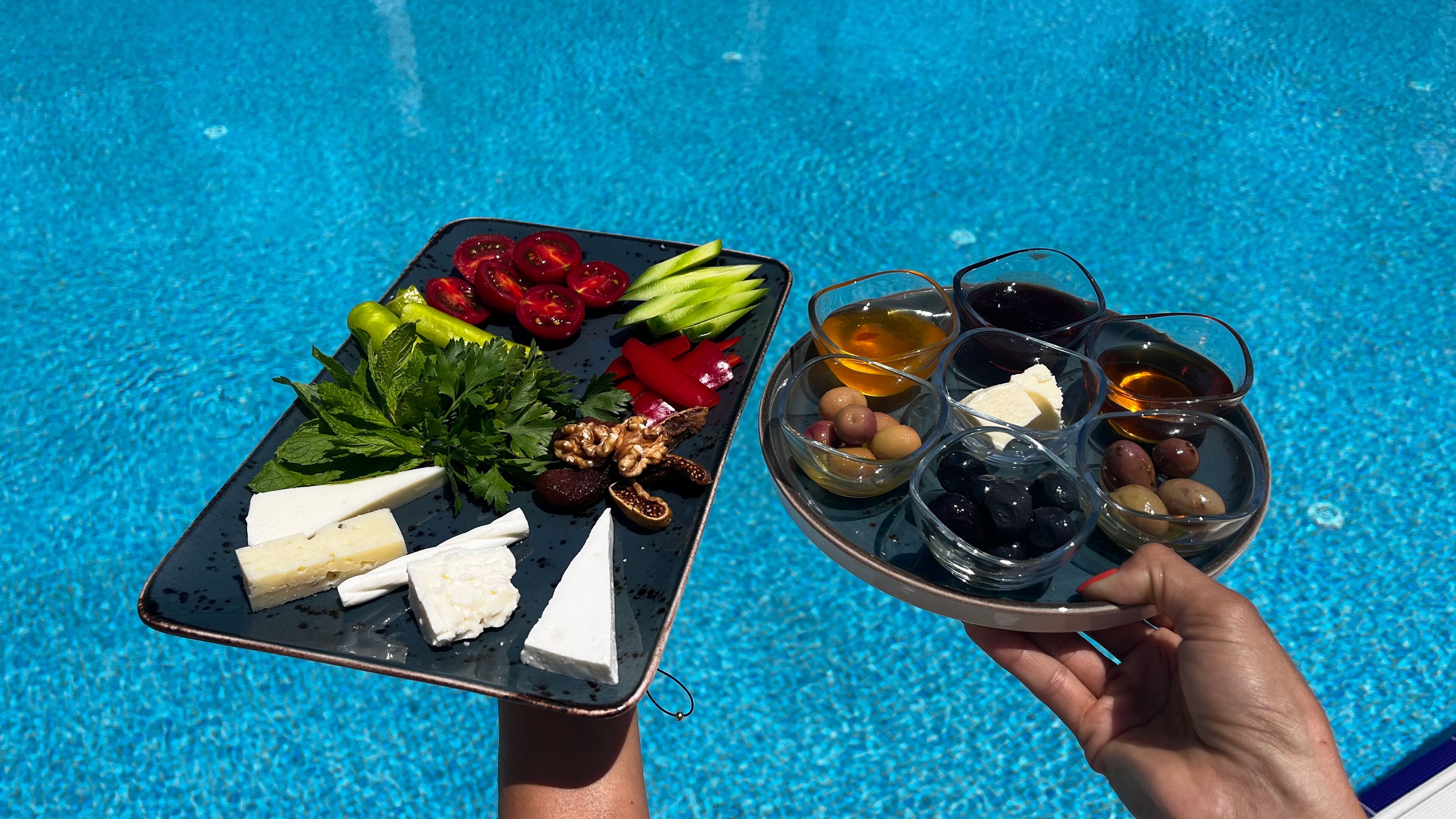 A tray with cheese, olives, and nuts by a pool.
